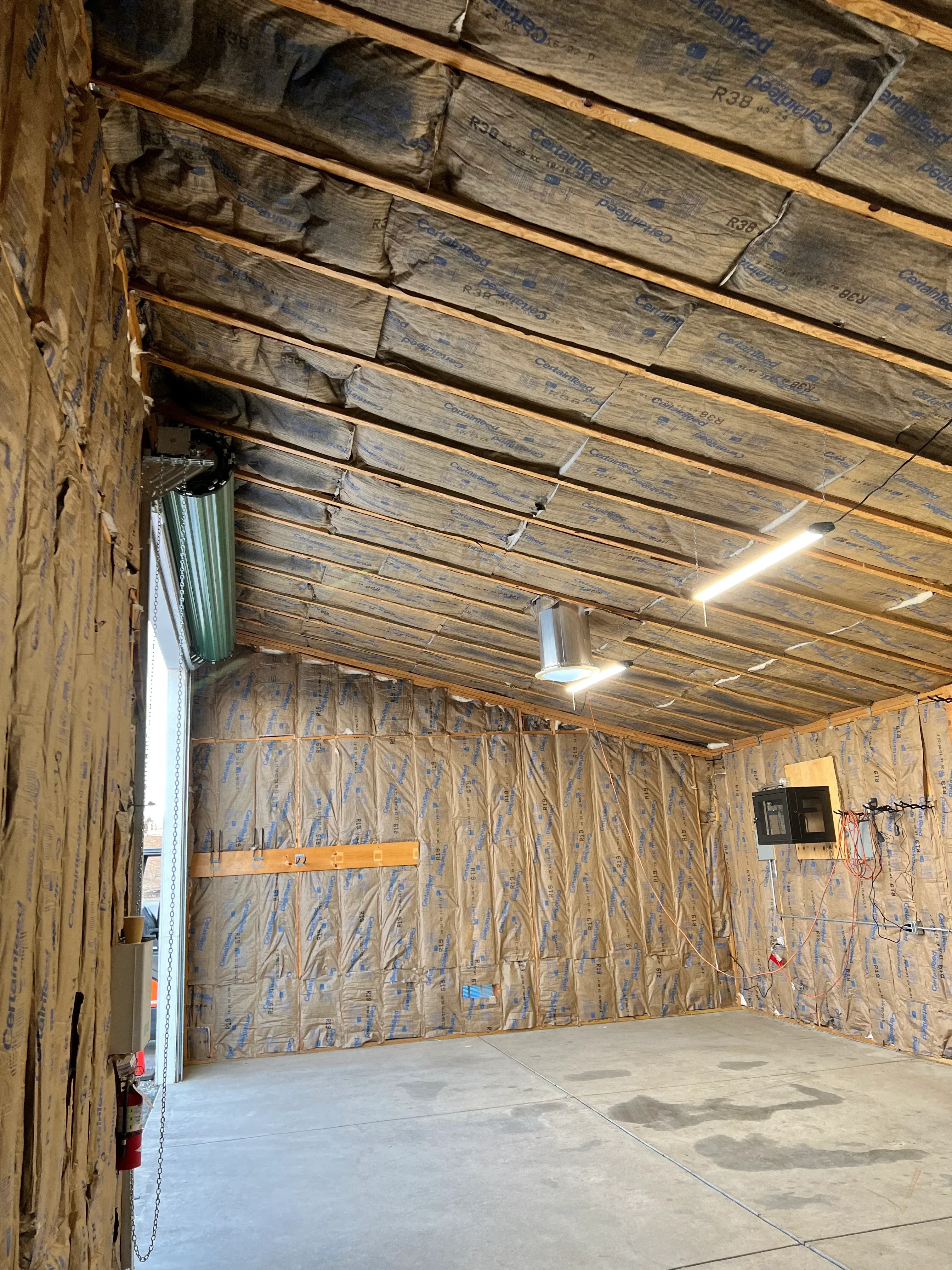 Fiberglass batt insulation installed between attic framing with vapor barrier and recessed light fixture