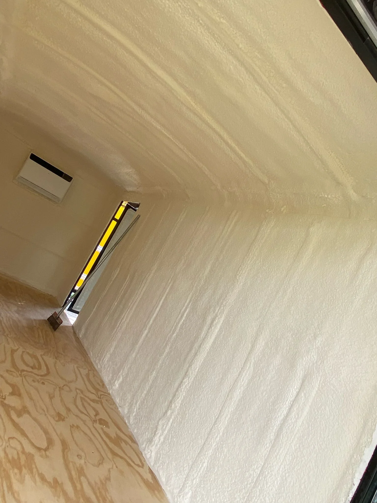 Blown-in fiberglass insulation installed in attic with yellow measurement tool and ventilation access