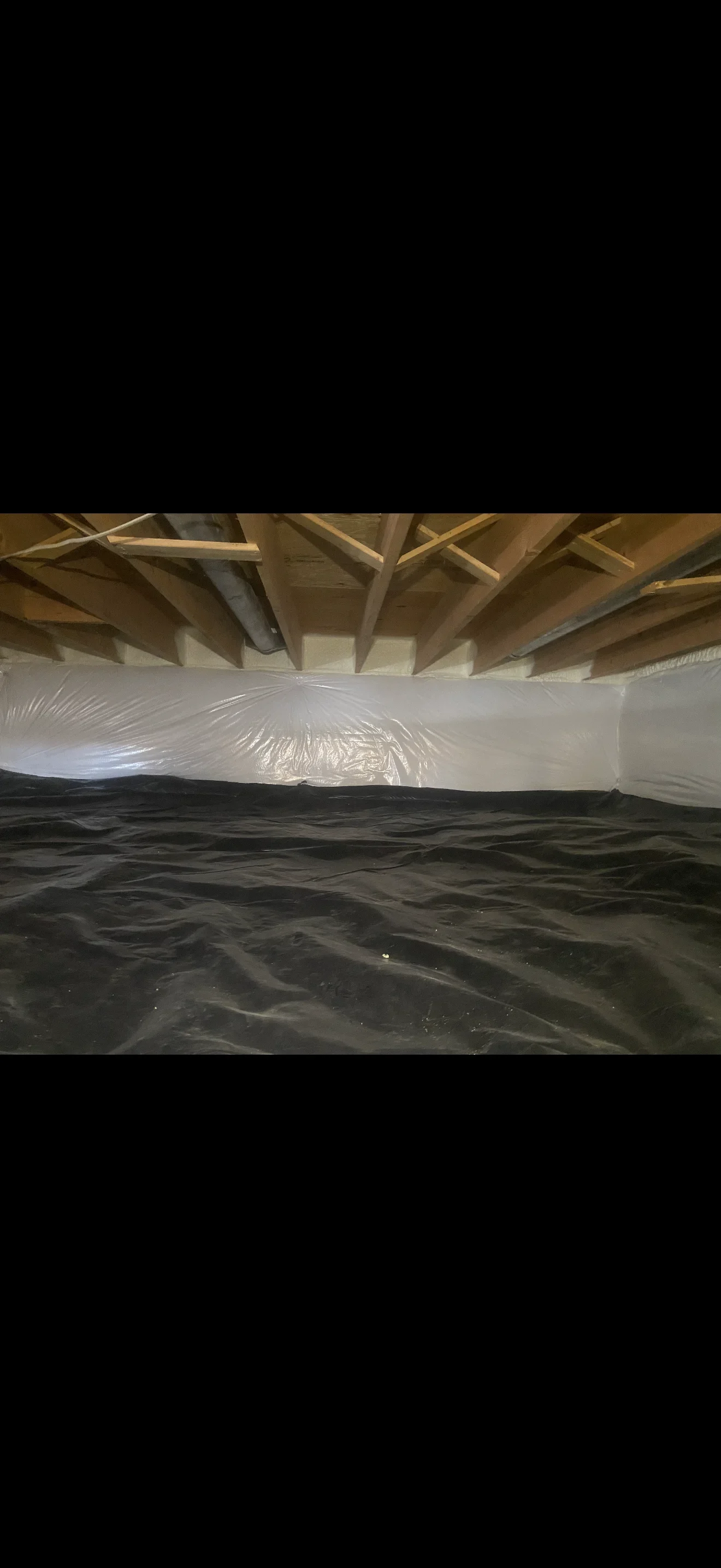 Crawl space with black polyethylene vapor barrier and white rim joist encapsulation under wooden floor joists