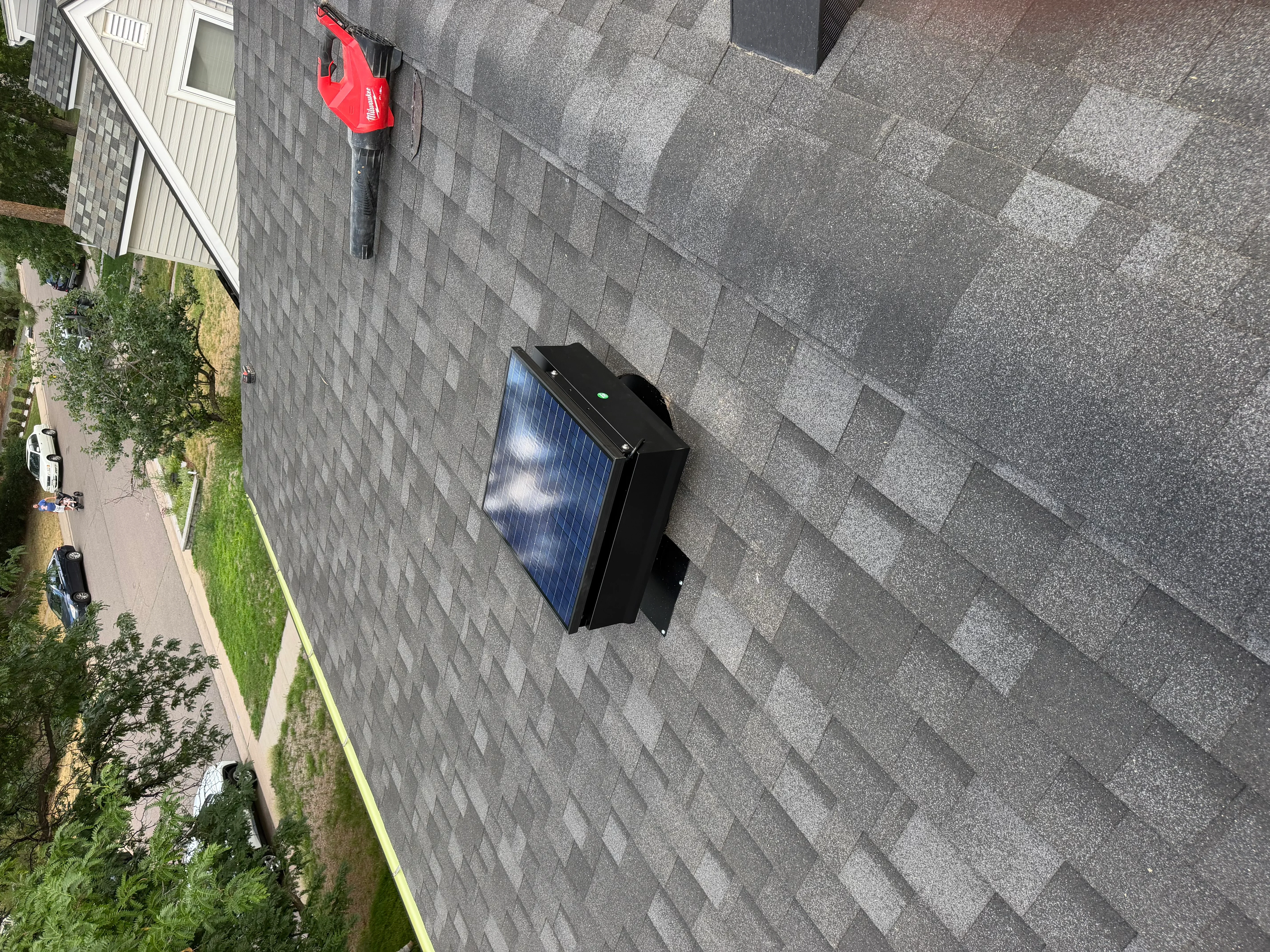 Solar attic fan with black bracket and blue solar panel mounted on gray asphalt shingle roof