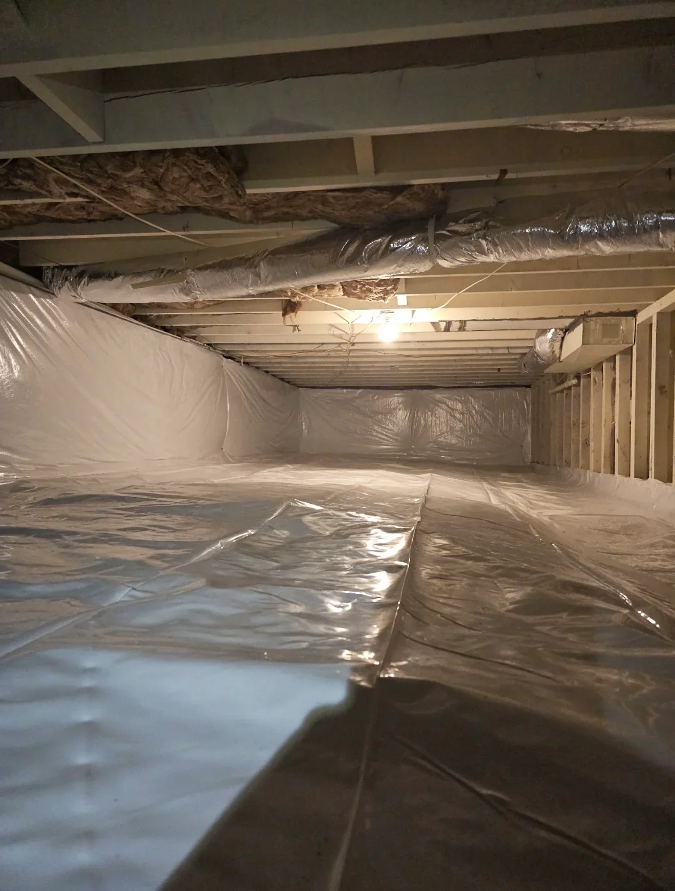 Crawlspace with polyethylene vapor barrier and wrapped fiberglass duct insulation on wooden joists