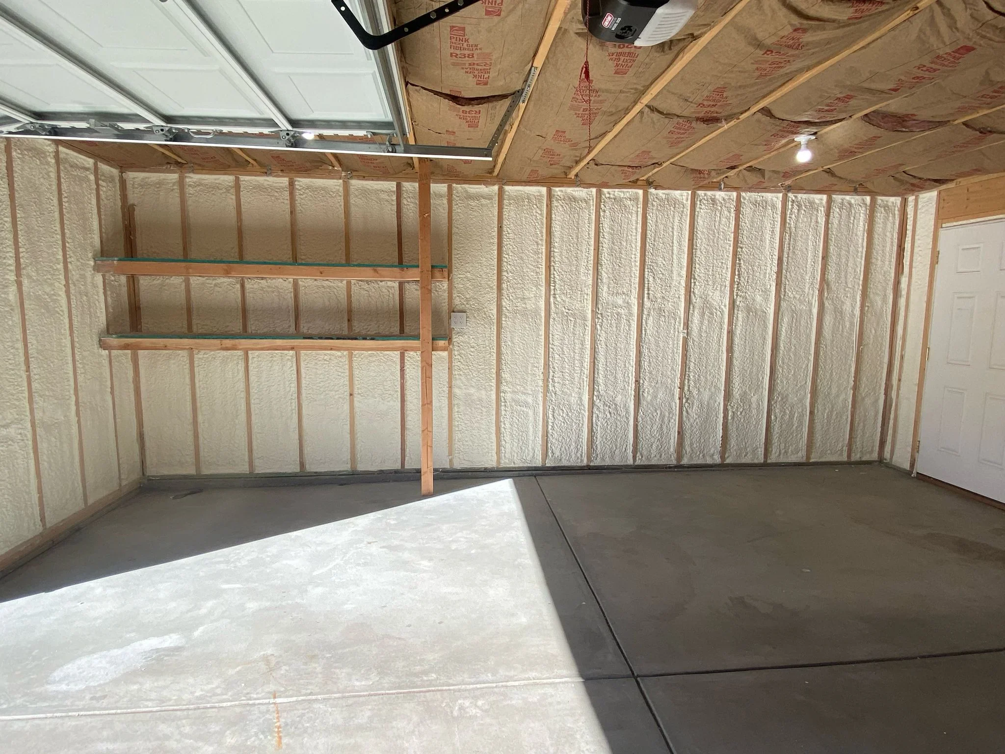 Garage interior with spray foam insulation in wall cavities and ceiling, wood framing, kraft paper vapor barrier